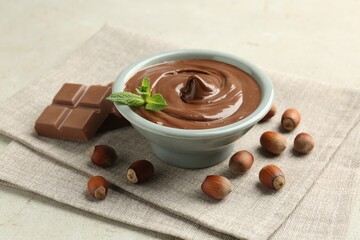 Tasty chocolate spread, pieces, mint and hazelnuts on light table, closeup
