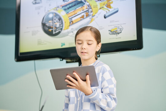 Child standing in front of large screen with schematic diagram, holding tablet in hand and presenting information to audience. Young student engaging in digital learning environment