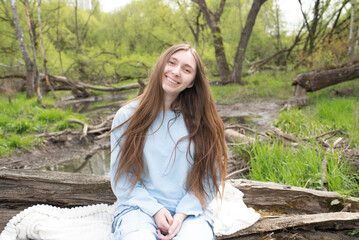 happy teenage girl or young woman sitting on log near river in park