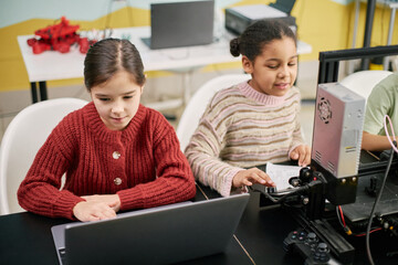 Two children sitting at desks engaging with laptops and educational tools. Creating a learning environment that sparks curiosity and enhances technical skills