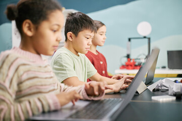 Children sitting at desks in classroom and using laptops for educational purposes. Focused...
