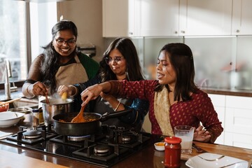 Three adult South Asian women, wearing colorful ethnic clothing, cook a traditional meal together...
