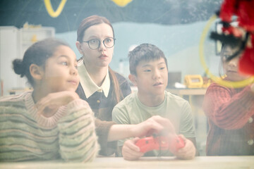 Multiracial children engaging in classroom activity with teacher observing closely Students using interactive equipment while being supervised by educator indoors