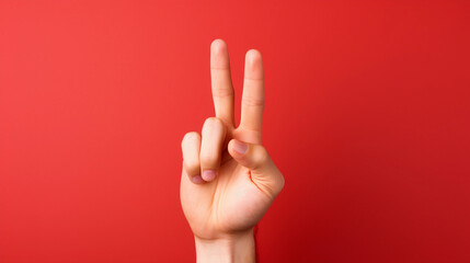 Close-up of a human hand making a two-finger gesture symbolizing the number two, peace, or victory, isolated against a plain solid color background in studio lighting