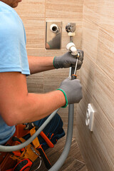 Plumber tightening drain hose connection of washing machine using screwdriver in modern bathroom
