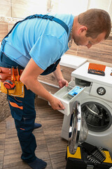 Plumber inspecting detergent dispenser while repairing domestic washing machine in bathroom