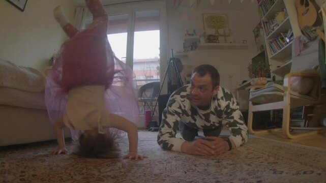 A child and an adult happily do handstands on a soft carpet, enjoying a joyful bonding activity