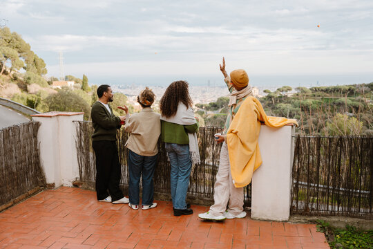 Group of four friends standing and holding cups while looking at landscape, outdoors