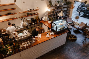 A female owner stands behind the bar and writes in a notebook while a male employee stands behind...