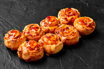 Delicious pizza rolls topped with melted cheese and spicy sauce resting on black stone surface