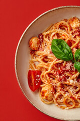 Delicious italian spaghetti with tomato sauce, meatballs and basil on red background