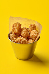 Tater tots overflowing a metal bucket on a yellow background