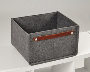 Empty grey felt storage box with leather handle sitting on white shelf