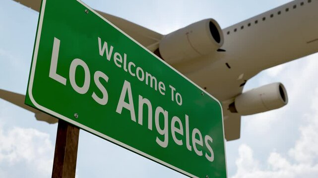 Welcome To Los Angeles Green Road Sign Against a Blue Sky and Clouds with Low Flying Airplane Above.