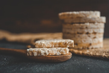 Stack of rice cakes on a rustic dark background with a couple placed on a wooden spoon in the foreground. Crisp, light, and healthy snack option styled naturally