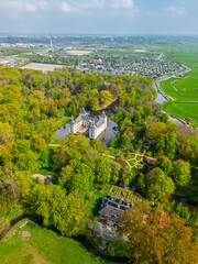 Aerial view of a historic castle surrounded by a forest, with vast green fields, winding waterways, and a river stretching across the flat Dutch countryside under a partly cloudy sky.