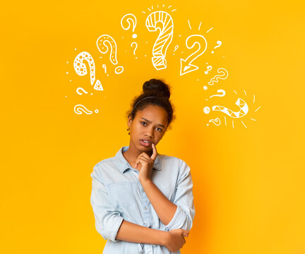 Puzzled pensive young african american teen girl in casual t-shirt posing over orange background with white question marks