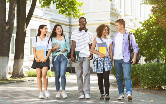 Happy university students walking together on campus, chatting and laughing outdoors during break, copy space