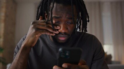 Close-up of young adult african man with sad expression after reading bad news from text message on his smartphone - Powered by Adobe