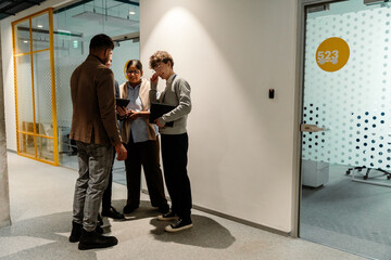 Group of three employees and a male intern stand and laugh while talking, in a hallway