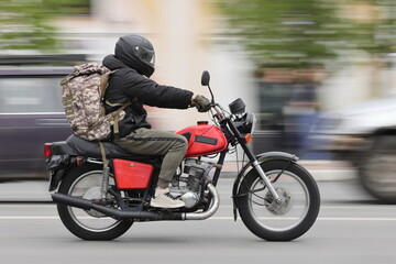 A man rides a red motorcycle along a city street