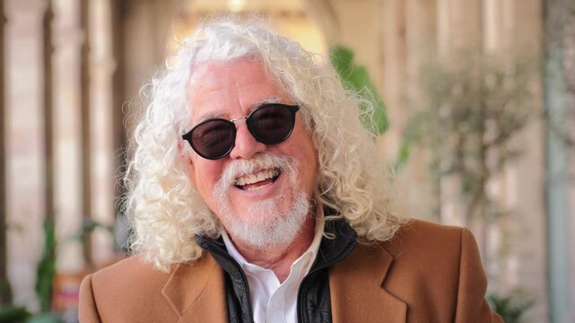 Cheerful mature man with curly hair and sunglasses expressing joy and warmth while sharing a delightful moment filled with laughter, happiness, and a bright smile that radiates positivity and
