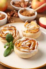 Tasty apple roses with powdered sugar served on table, closeup