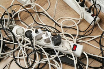 Extension power boards overloaded with plugs on wooden floor, closeup