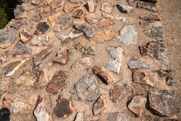 Detail of an old stone path under bright sunlight, showing irregular rocks embedded in dry soil. Captured during summer in a rural area, highlighting rustic textures and natural materials.