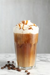 Tasty iced coffee with whipped cream, syrup and beans on white marble table