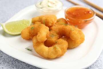 Tasty tempura shrimps, lime and sauces on grey textured table, closeup