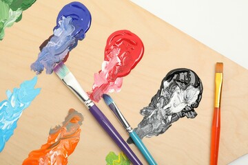 Wooden palette with paints and brushes on white background, top view