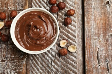 Chocolate hazelnut spread in bowl and nuts on wooden table, flat lay. Space for text