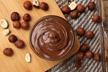 Chocolate hazelnut spread in bowl and nuts on wooden table, flat lay