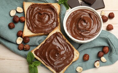 Toasts with chocolate hazelnut spread, nuts and mint on wooden table, flat lay