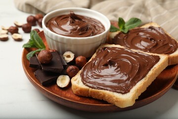 Toasts with chocolate hazelnut spread, nuts, pieces of chocolate and mint on white marble table, closeup