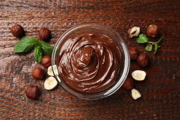 Chocolate hazelnut spread in bowl, nuts and mint on wooden table, flat lay