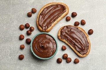 Toasts with tasty chocolate hazelnut spread and nuts on grey table, flat lay