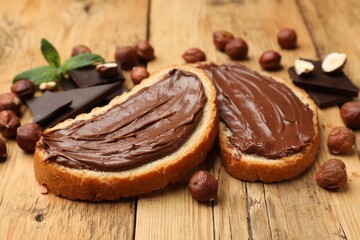 Toasts with tasty hazelnut spread, chocolate pieces and nuts on wooden table, closeup
