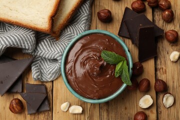 Tasty hazelnut spread with mint, chocolate pieces and nuts on wooden table, flat lay