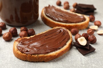 Toasts with tasty hazelnut spread, chocolate pieces and nuts on grey table, closeup