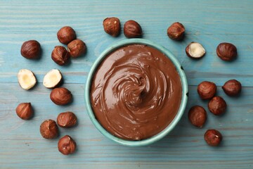 Tasty chocolate hazelnut spread and nuts on blue wooden table, flat lay