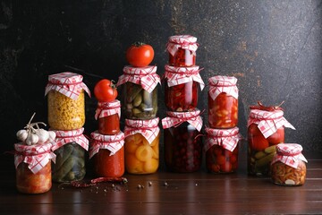 Many jars with different pickled products and ingredients on wooden table