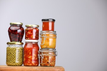 Many jars with different pickled products on wooden board against light grey background, space for text