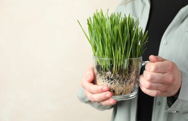 Woman with wheat grass in transparent pot on light background, closeup. Space for text