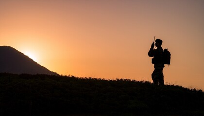 Silhouette of a soldier communicating in the mountains with military communication equipment
