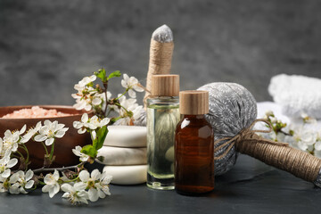 Spa composition with cosmetic products and beautiful flowers on black textured table, closeup