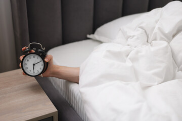 Sleepy man with alarm clock in bed indoors