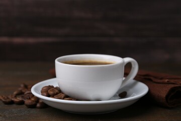 Aromatic coffee in cup, beans and saucer on wooden table, closeup