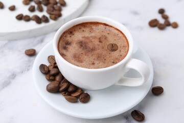 Aromatic coffee in cup, beans and saucer on white marble table, closeup
